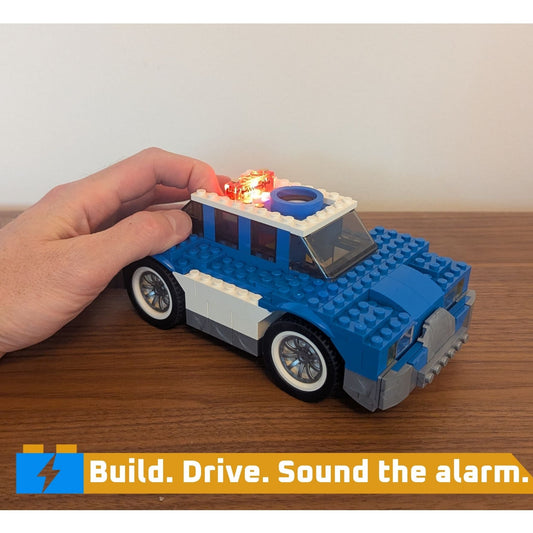 A hand pressing a button on a motorized patrol car built from an electronic building kit to activate the lights, demonstrating a screen-free STEM toy and circuit building toy.