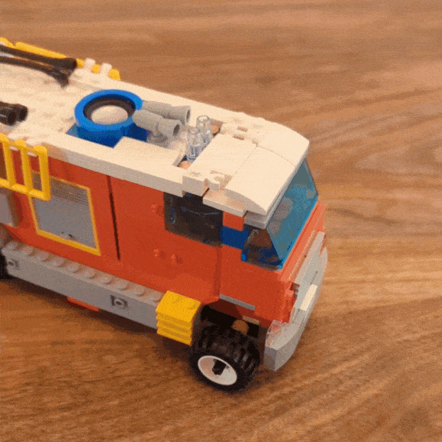 A young hand flipping up the lid of a toy fire truck to slide a switch and turn on lights on the truck