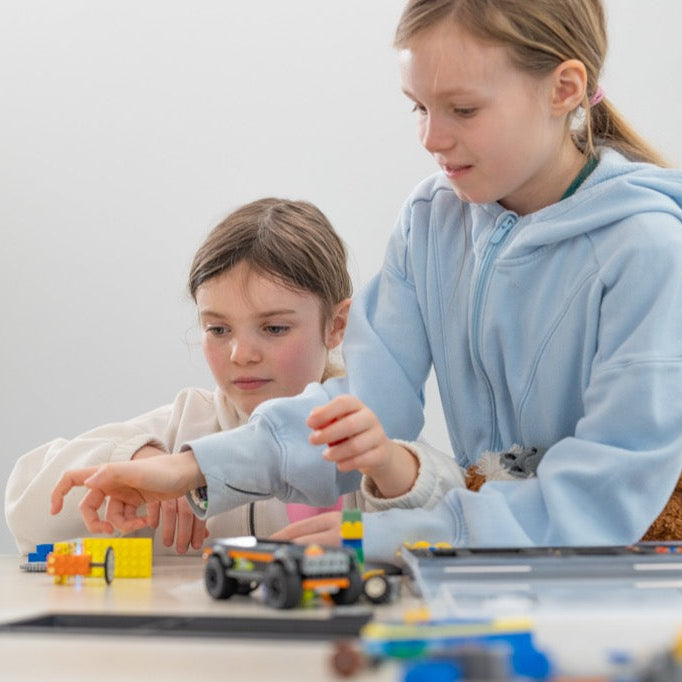 Two students collaborating on a smart classroom kit project using electronic building blocks to build motorized vehicles for screen-free learning.