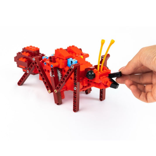 Red and brown LEGO-brick-like creature being played with by a hand on a white background