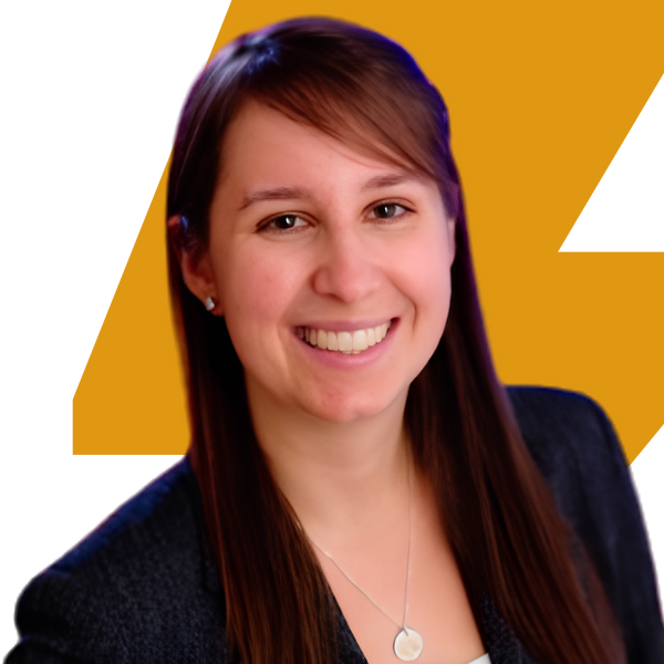 A smiling woman with long brown hair, wearing a dark blazer and a silver pendant necklace, set against a graphic background featuring a large yellow 'Z' on a white and black shape.