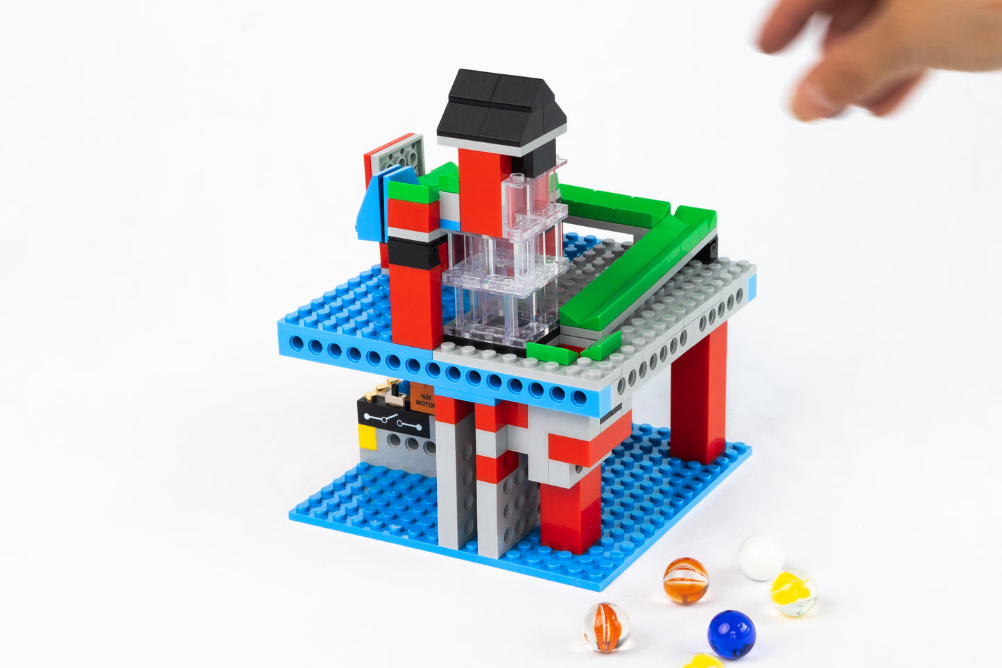 Colorful toy building set of a functional infinite loop marble run with a hand reaching towards it on a white background