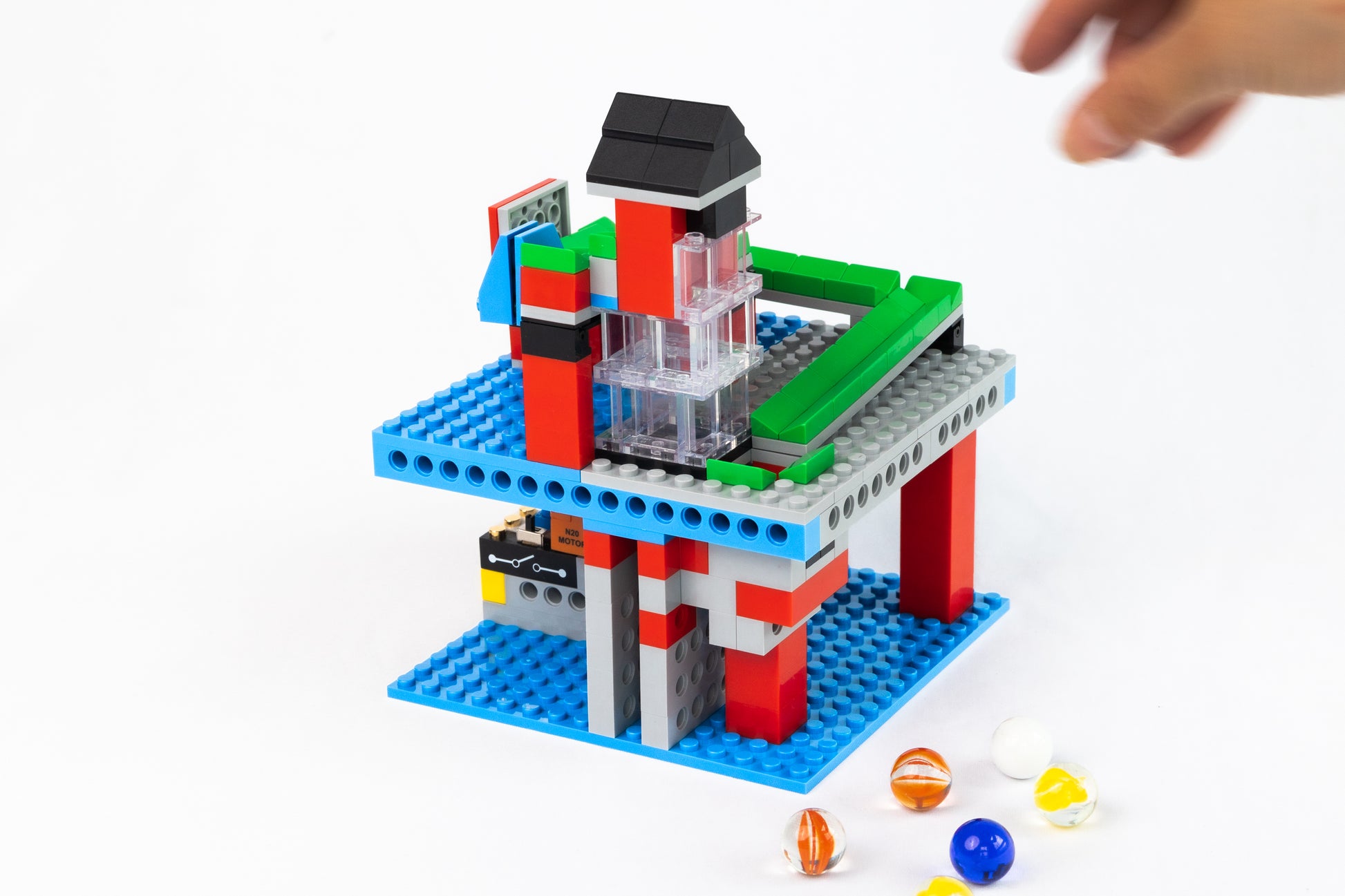 Colorful toy building set of a functional infinite loop marble run with a hand reaching towards it on a white background