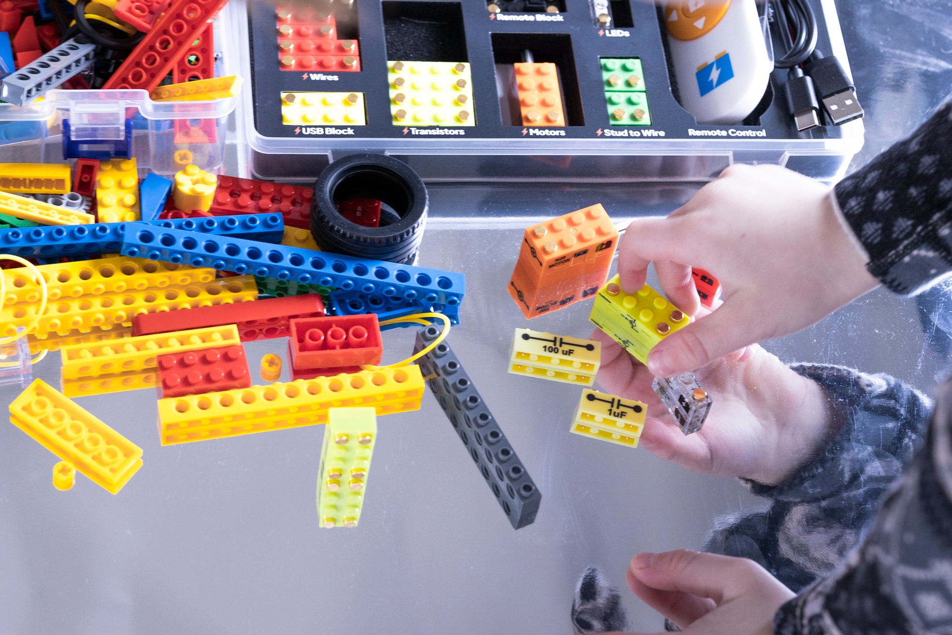 Colorful building blocks with a hand interacting with them on a gray surface.