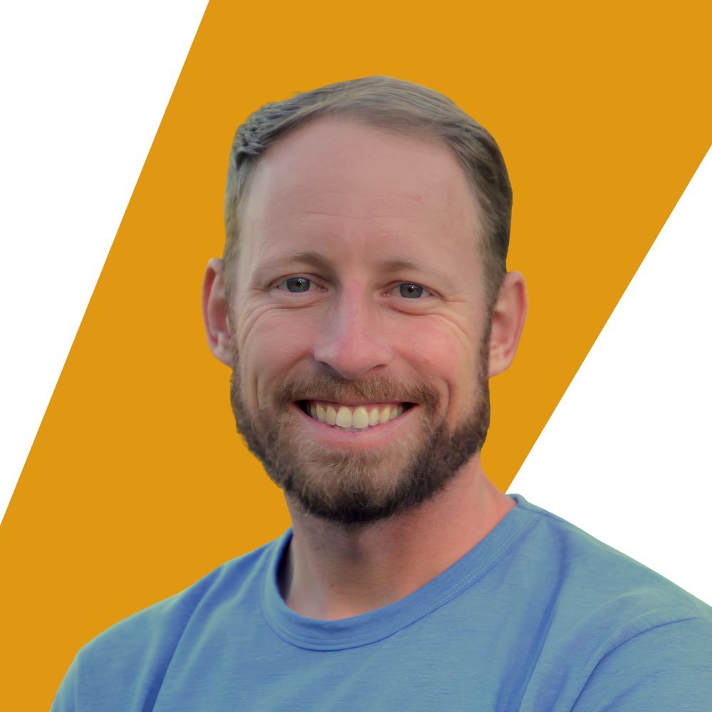 A smiling man with short light brown hair and a beard, wearing a light blue crewneck t-shirt, set against a graphic background of diagonal yellow and white shapes.