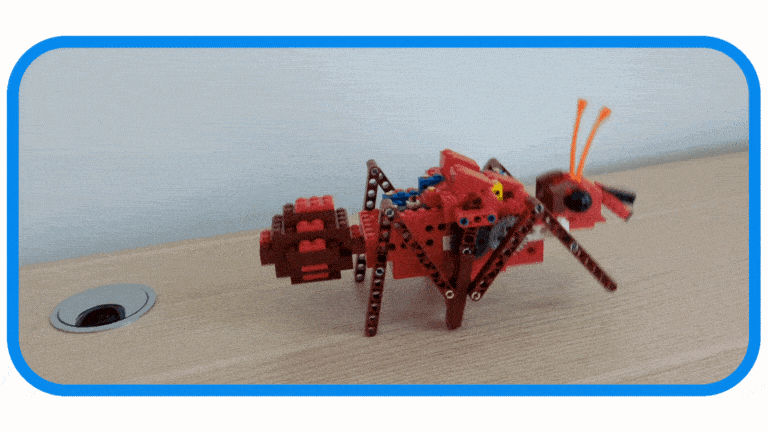A motorized 6-legged walking ant from the ultimate theme bundle  walking across a wooden table toward a daisy in a mug, showcasing a screen free educational toy and circuit building toy in action.