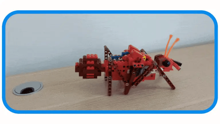 A motorized 6-legged walking ant from the ultimate theme bundle  walking across a wooden table toward a daisy in a mug, showcasing a screen free educational toy and circuit building toy in action.