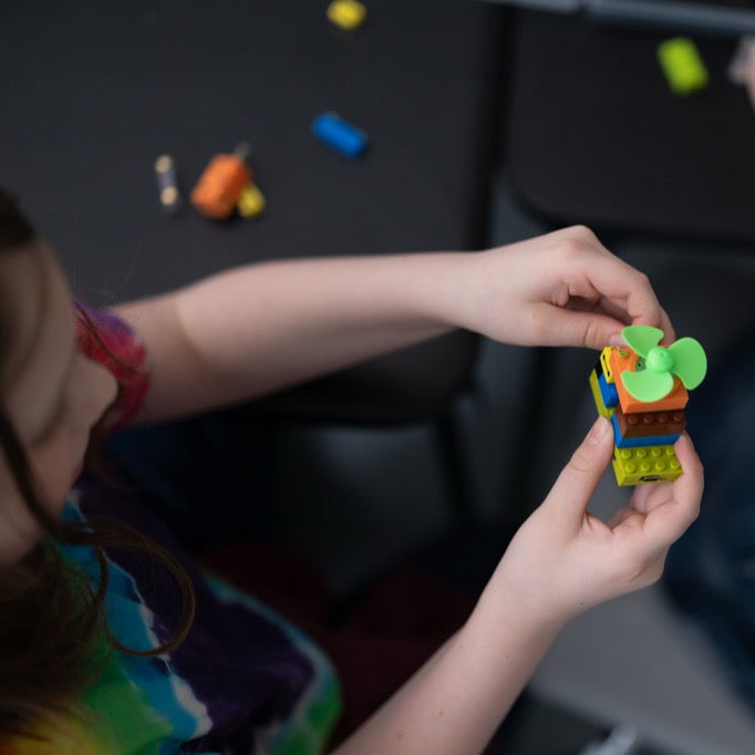 A hand holding a motorized green propeller module from a smart classroom kit, showcasing the functional electronic building blocks used in a classroom circuit kit.